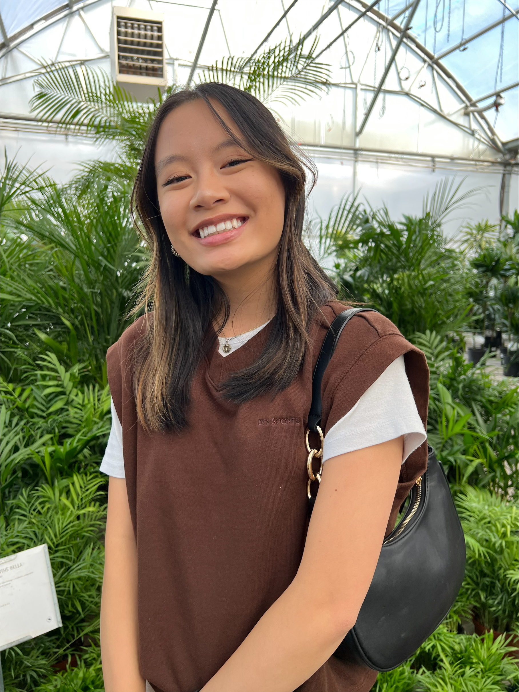 young woman in sweater vest smiling in front of greenery