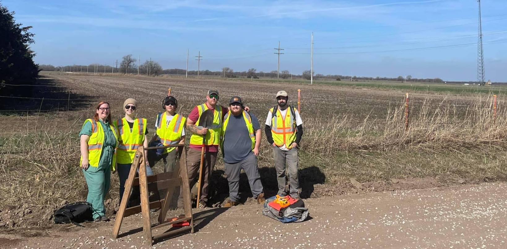 a small group of archaeologists wearing safety vests stand in front of an open field
