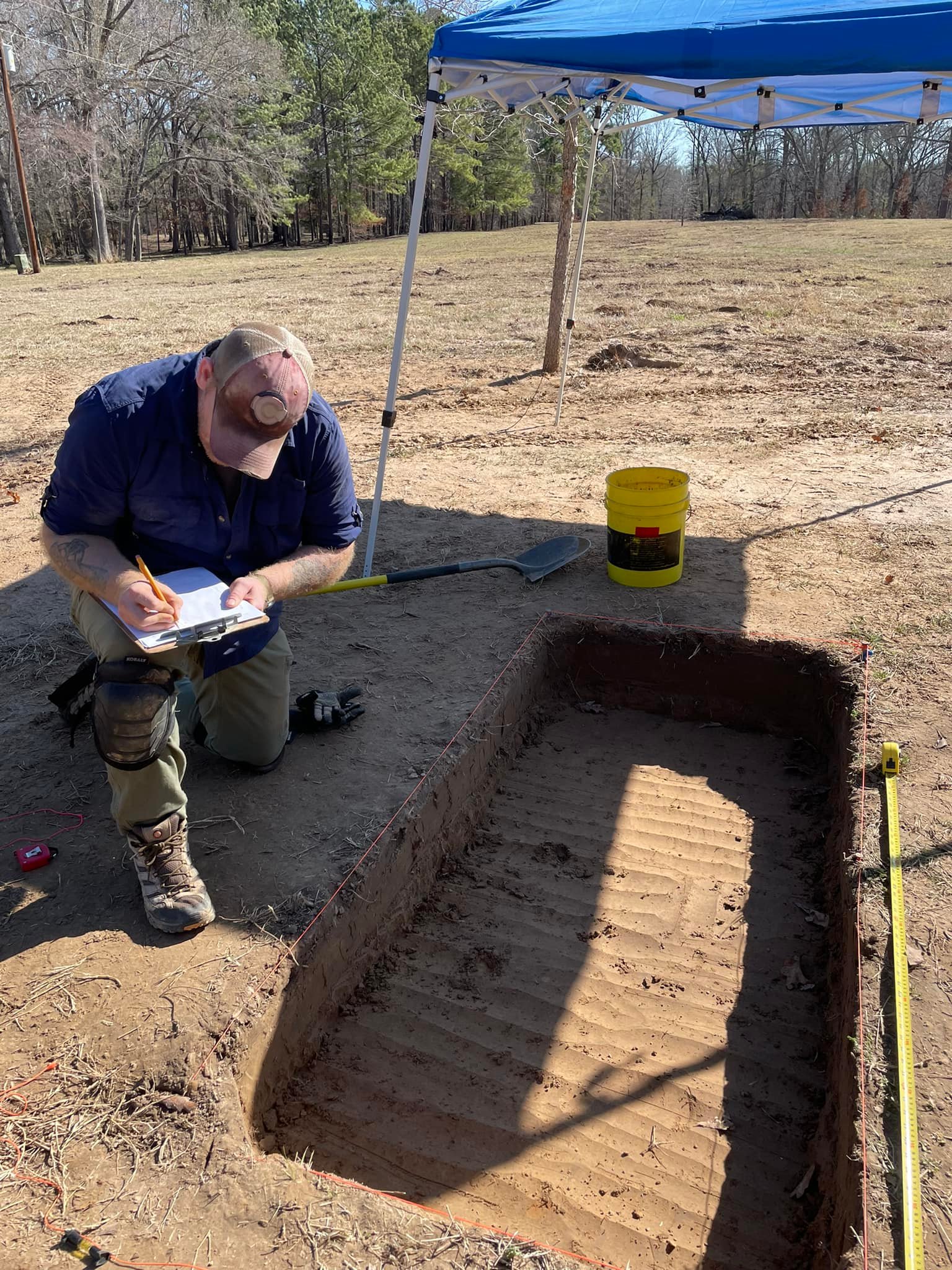 man kneeling taking notes by square hole