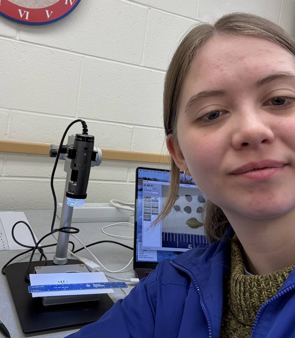 young white woman with blonde hair in front of microscope