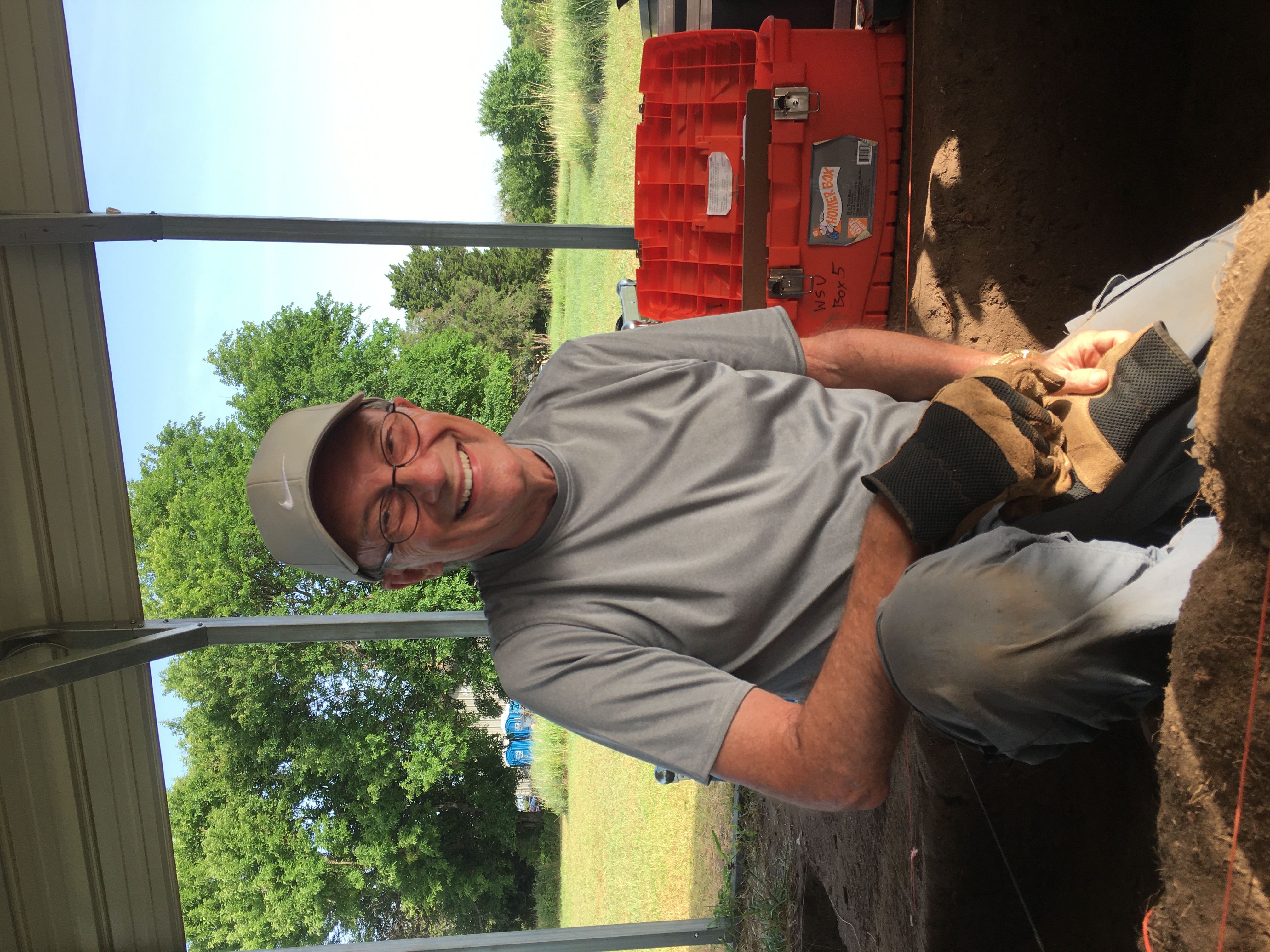 older man sitting in a pit holding a trowel