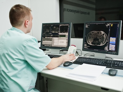 Radiation therapist overlooking treatment in MRI machine from computer