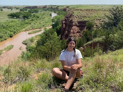 Student sitting on bluff surrounded by tall grass