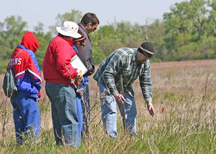 Group of students standing in a field, observing the native plant species