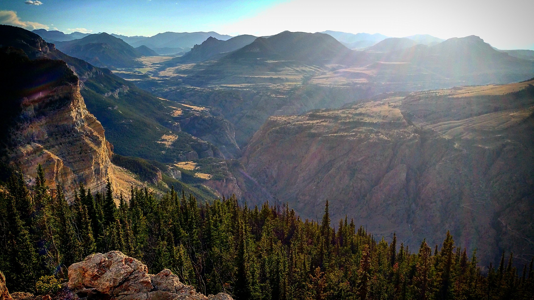 Sun shining down on a vista of a rocky valley dotted with pine trees