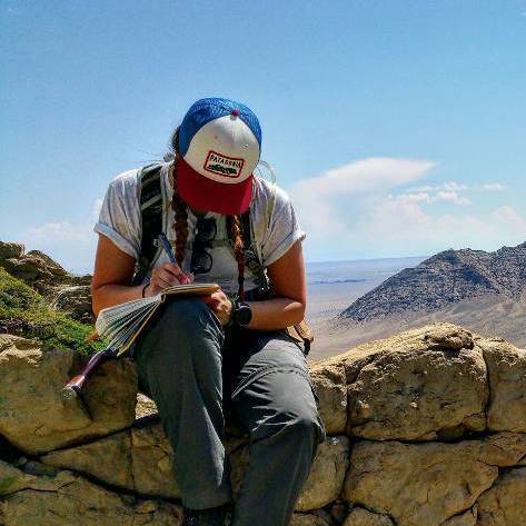 Geology student logging notes while seated on a low stone wall