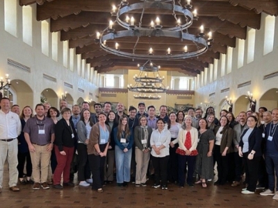 The EFCN team poses for a photo in a larger foyer with white columns and a large rustic chandilier hanging above.