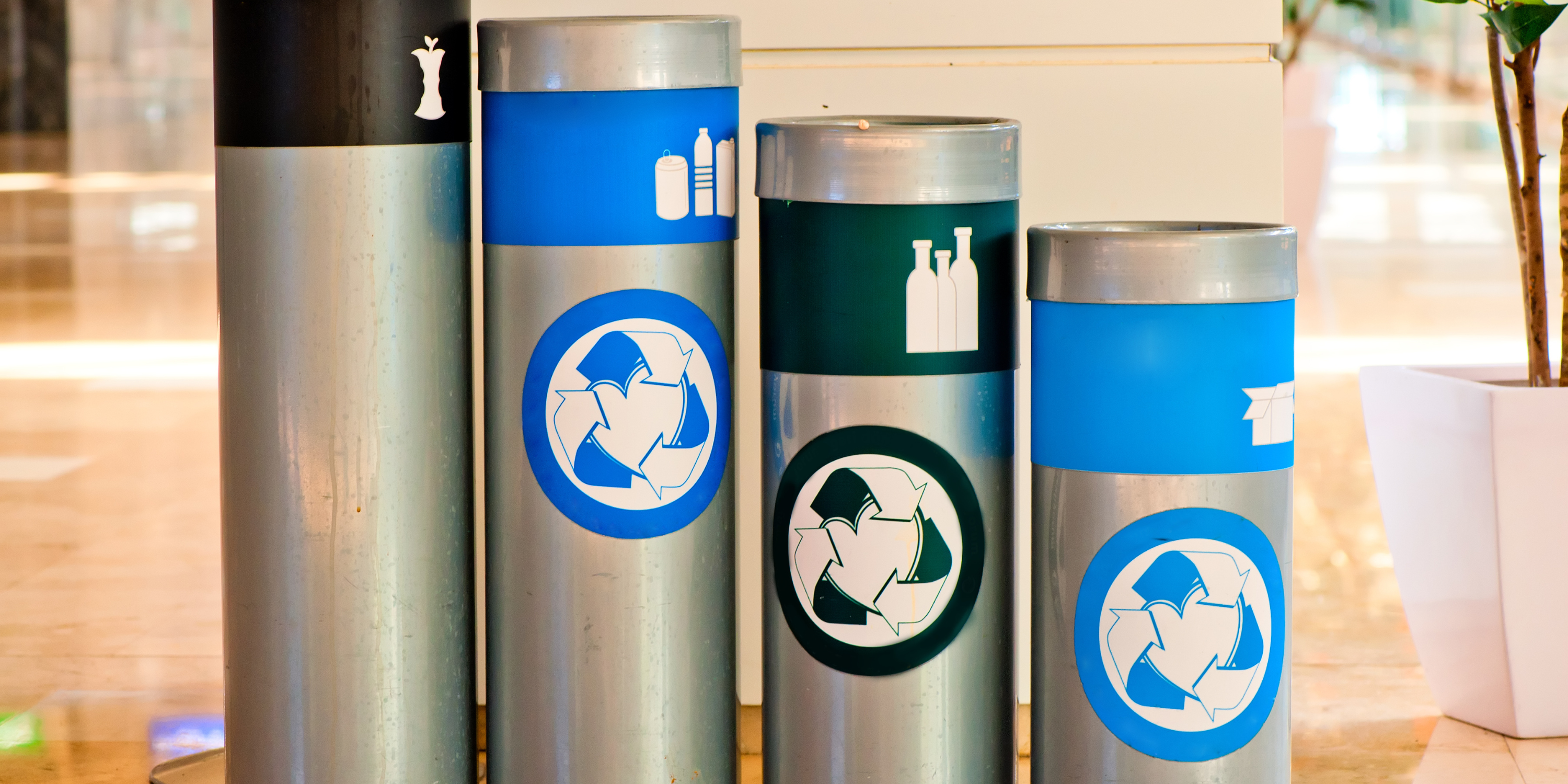 Four metal canisters used for waste disposal.  One is for food waste. One is for plastics.  One is for glass. One is for paper.