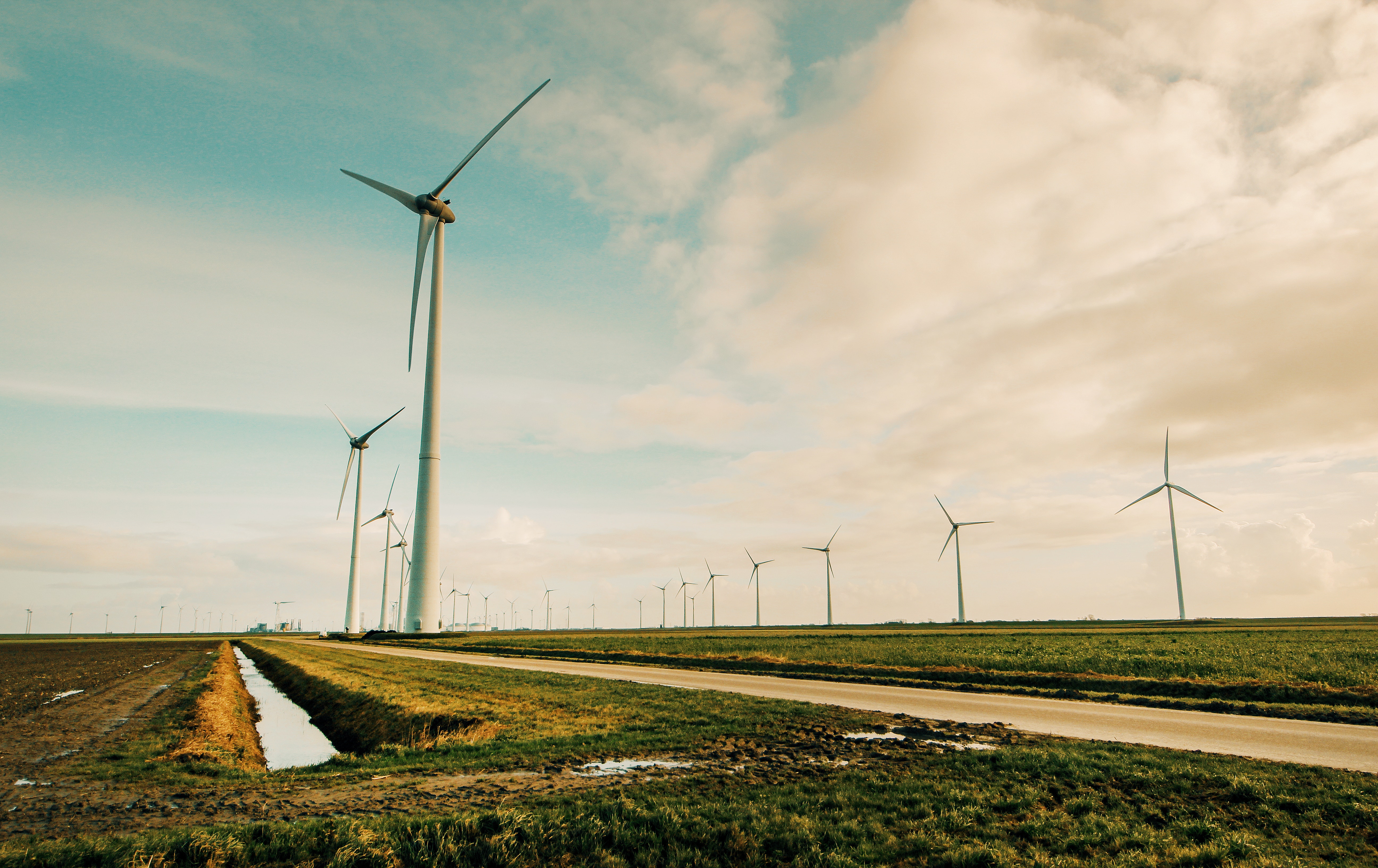 field with water in ditch and tall wind turbines against a cloudy sky