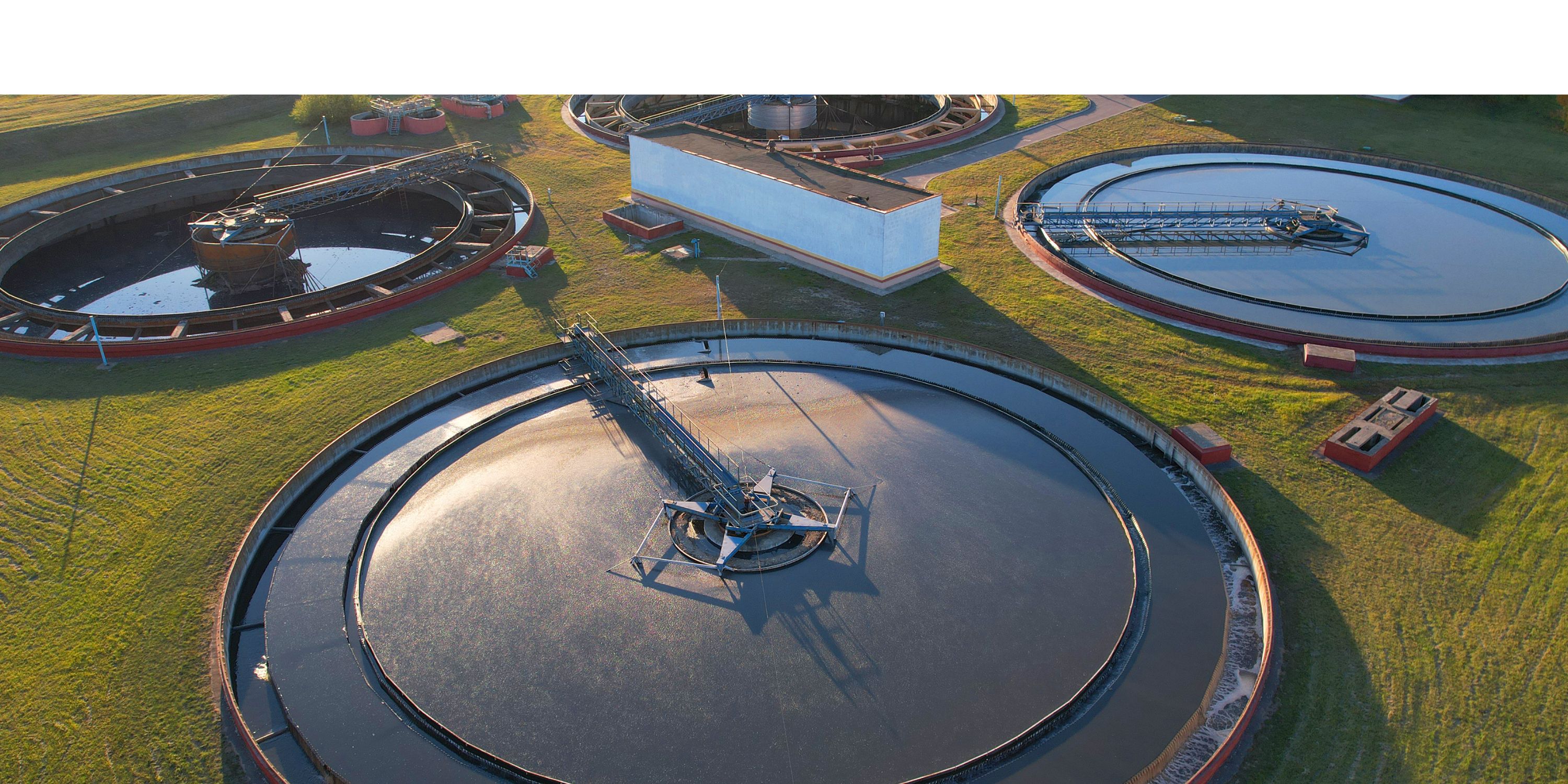 Aerial view of a water treatment plant with three circular clarifier tanks filled with water surrounded by green grass