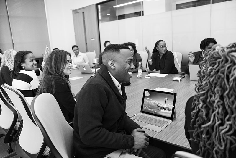 black and white photo of people gathered around table in board room for meeting.