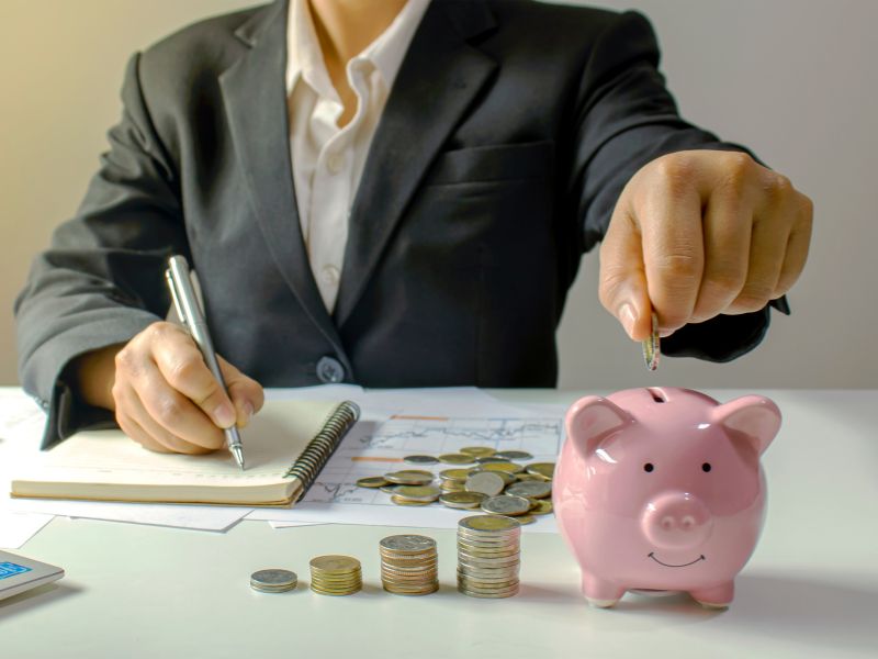 working professional at desk with notepad and pen, financial projections, coins and a piggy bank