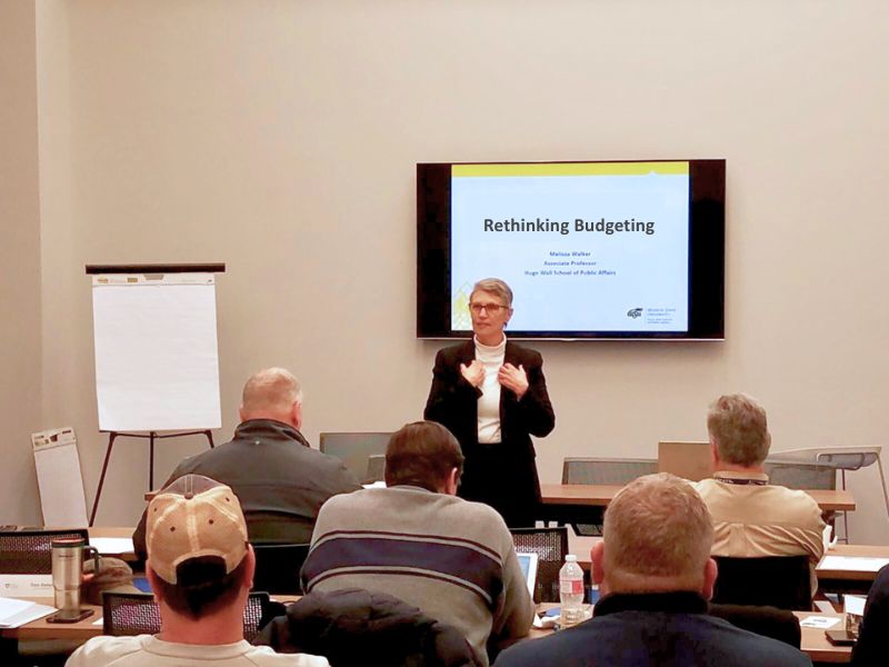 Speaker presents at front of conference room of attendees