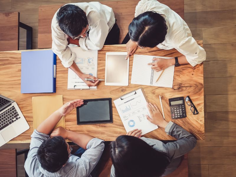 group of colleagues sitting at a table working on a project with charts, calculator, pens and paper
