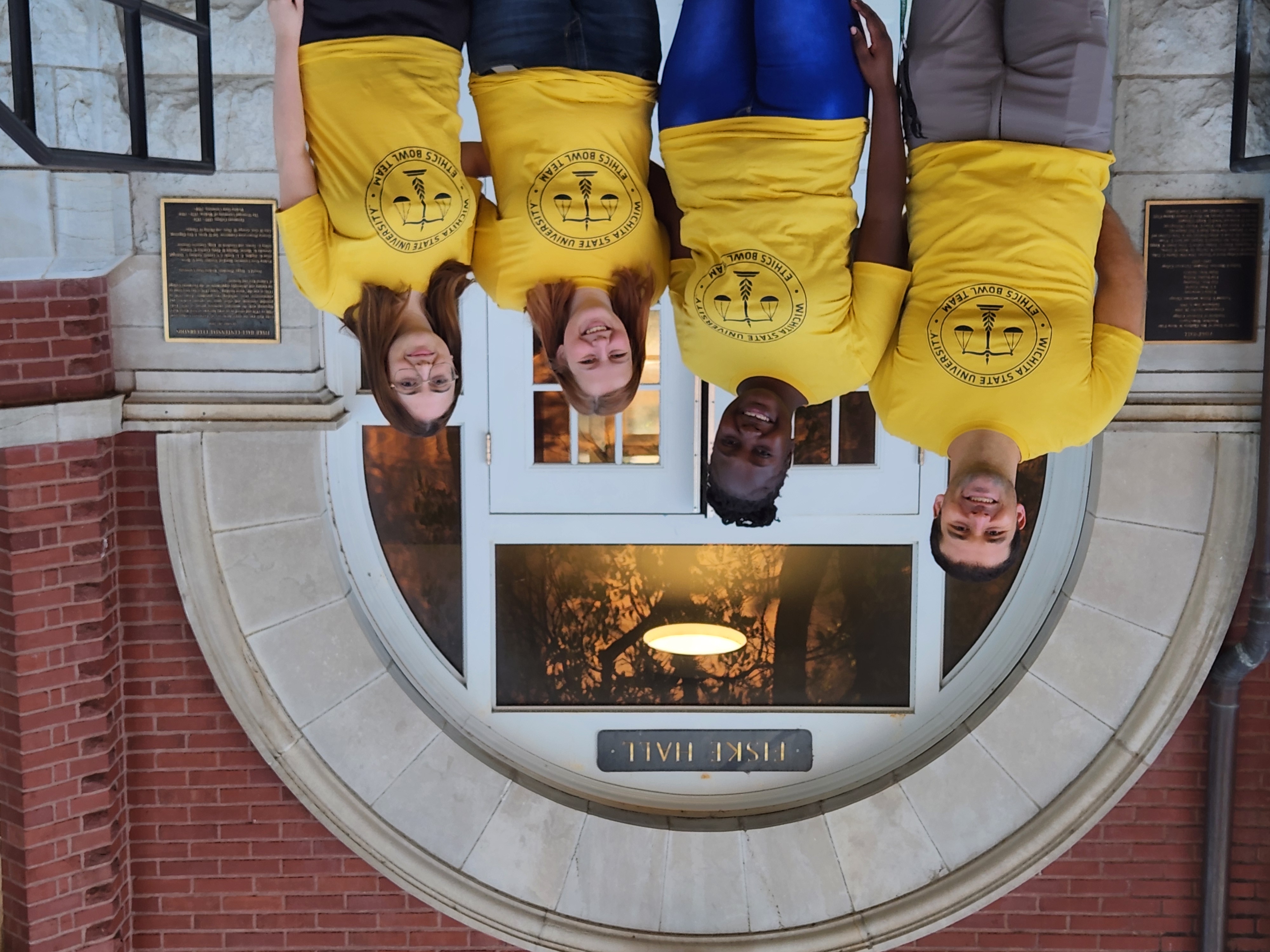 Photo of Dr. Colby Clark, Cynthia, Isla, and Monique wearing their Ethics Bowl t-shirts in front of Fiske Hall