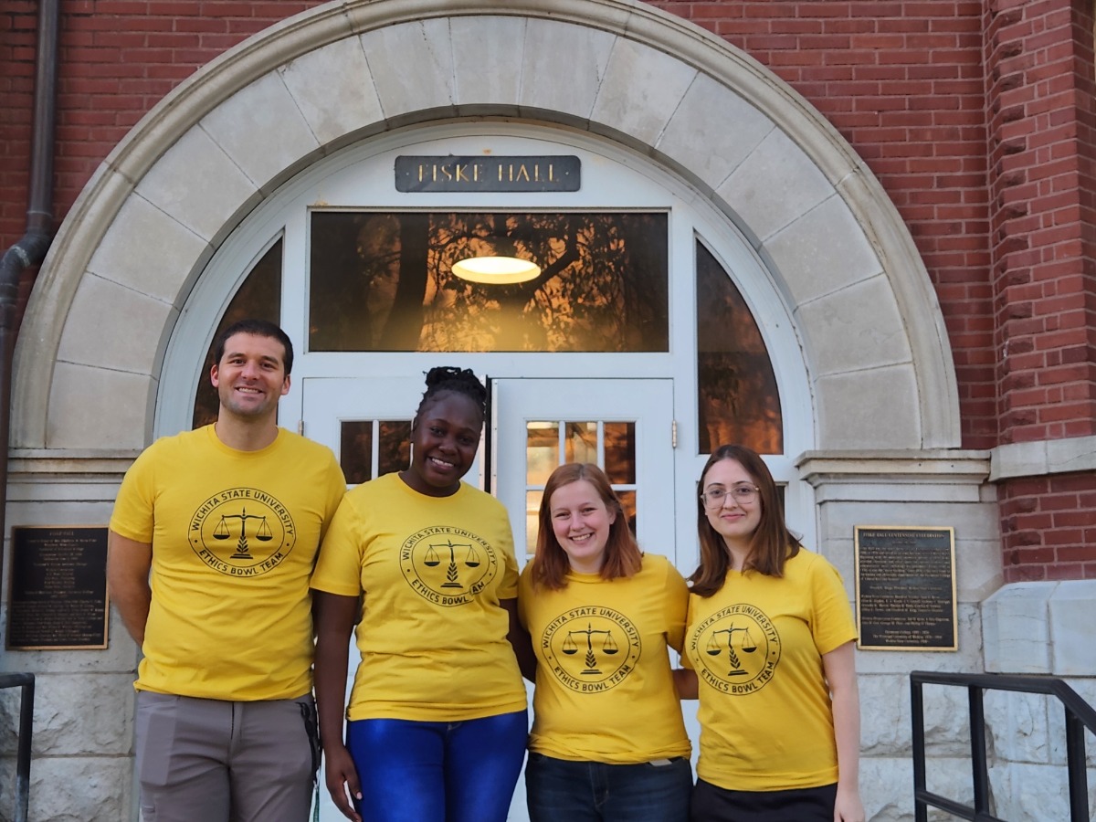 Photo of Dr. Colby Clark, Cynthia, Isla, and Monique wearing their Ethics Bowl t-shirts in front of Fiske Hall