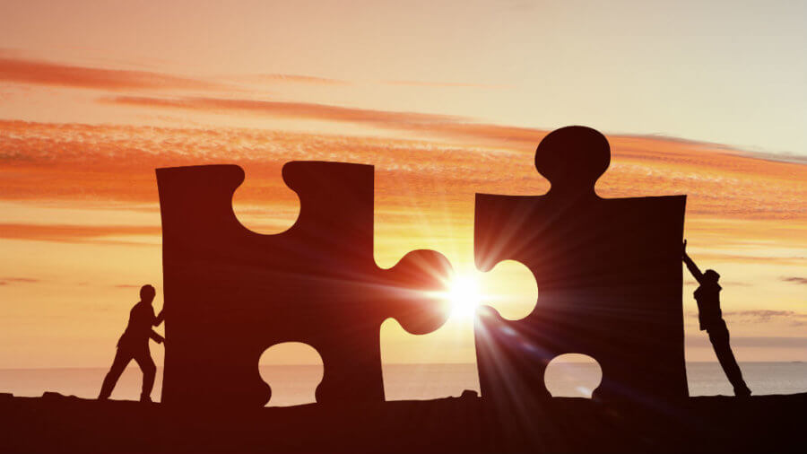 Two people in shadow pushing together two giant puzzle pieces