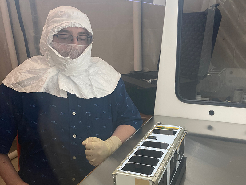 A student wearing protective gear poses with a CubeSat nanosatellite