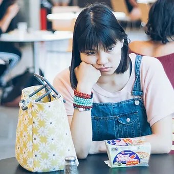 A student looks sad while sitting alone at a school lunch table.