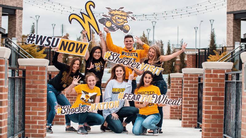 group photo, holding various signs for WSU saying "#WSU Now, Fear the Wheat, Shocker nation"