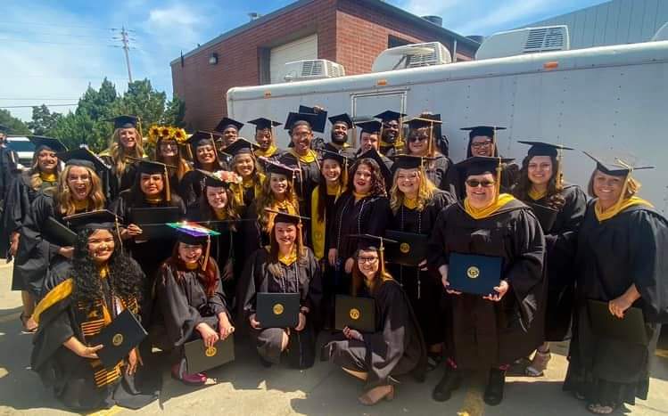 School of Social work graduates standing in a group smiling in their cap and gowns