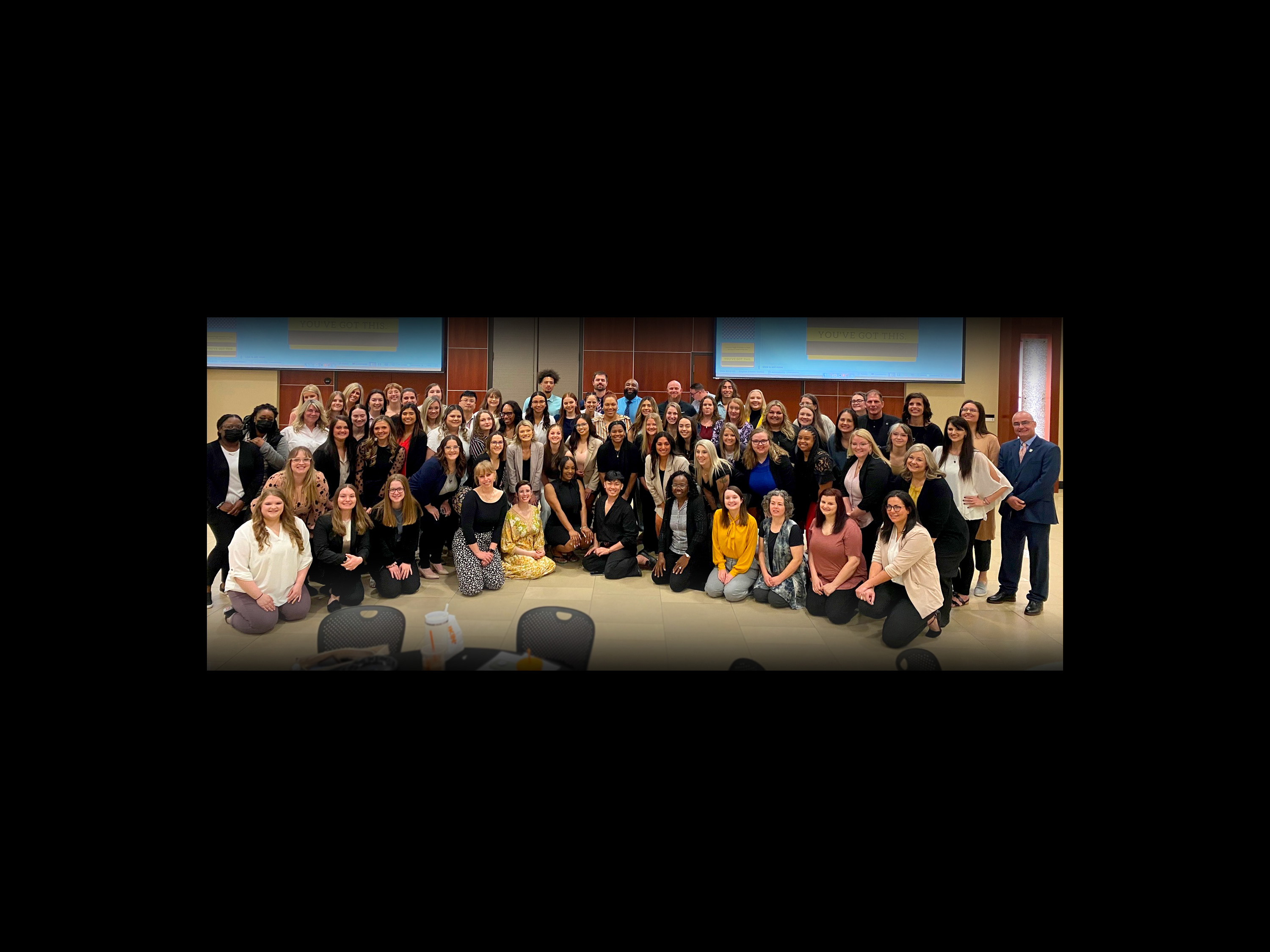 A large group of social work students poses for a photo in the Rhatigan Student Center ballroom.