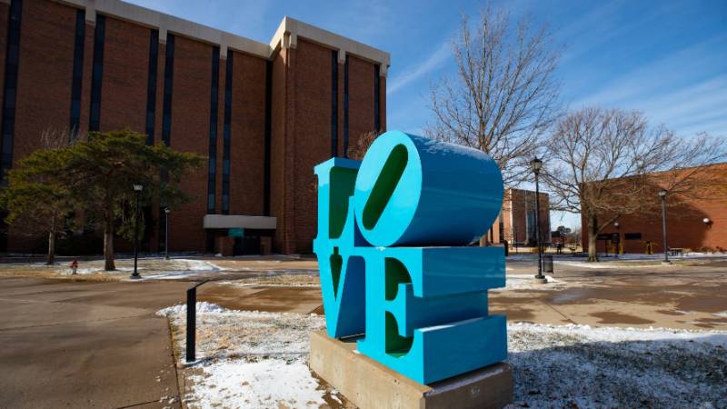 "LOVE" statue with snow on the ground, with Lindquist Hall in the background