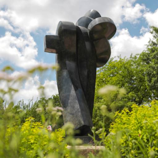 Danseuse Espagnole (Spanish Dancer) by artist Sophía Vári. Abstract bronze sculpture with flowing, interlocking shapes, standing as the centerpiece of the Plaza of Heroines, surrounded by lush greenery under a partly cloudy sky. 