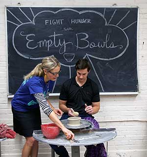 Brenda Lichman assists a volunteer working with clay at a pottery wheel at an Empty Bowls Wichita build-a-bowl workshop.