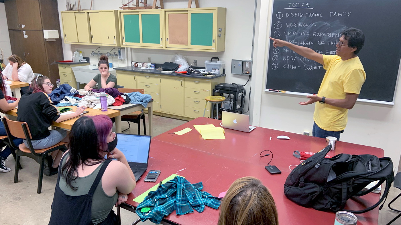 A picture of a classroom with a man at a blackboard surrounded by students. 