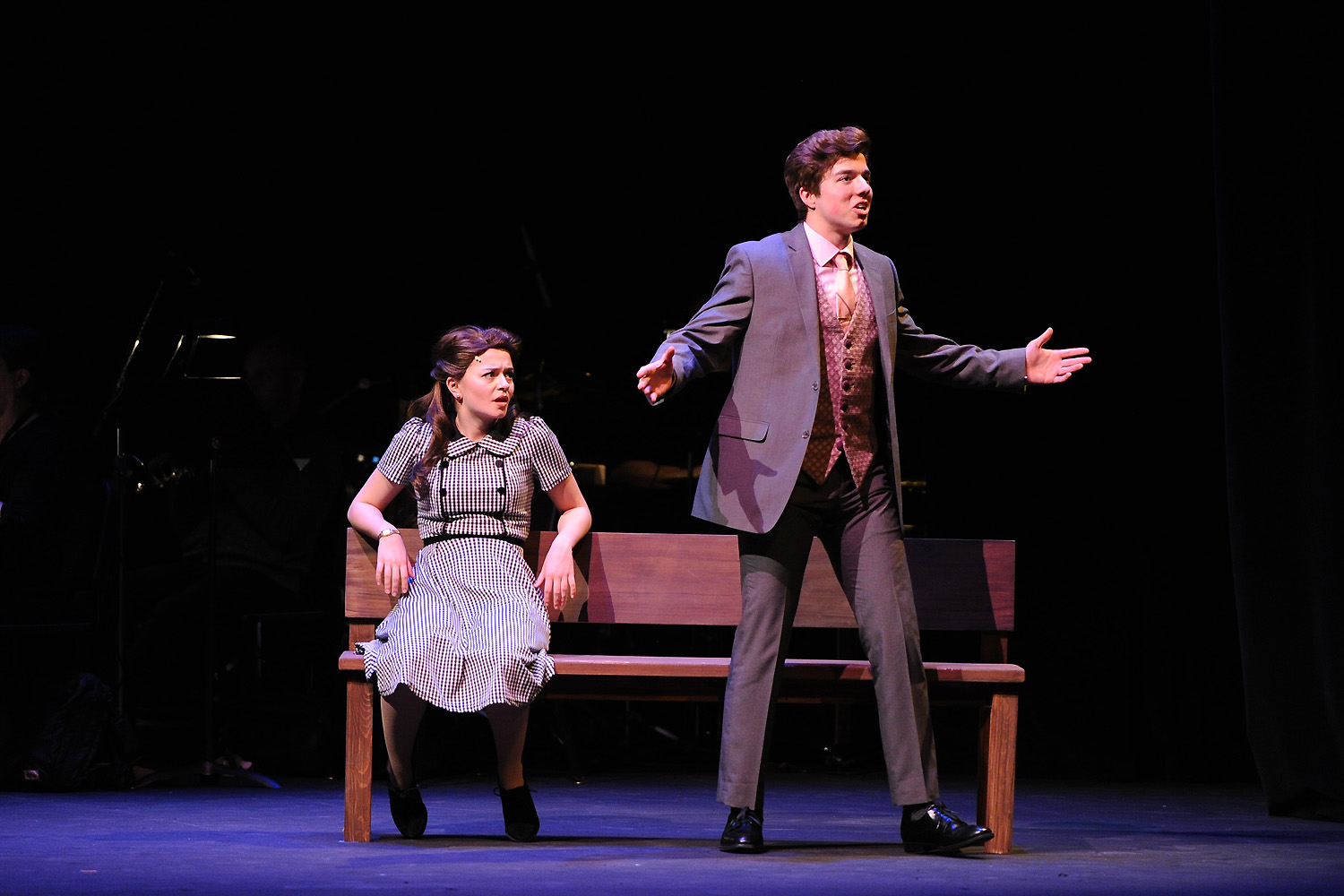 An actor and actress onstage during a performance with a strong spotlight and dark background.