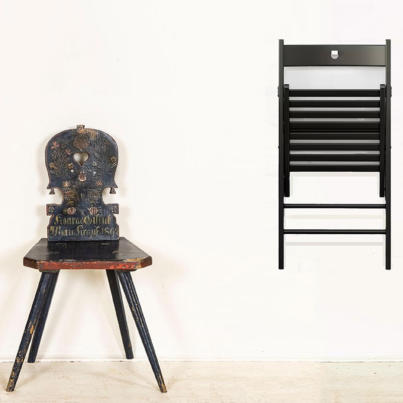 A photo of two different kinds of chairs against a white wall. One chair is folded and hanging on the wall, while the other is sitting on the floor to the left of the haning chair.