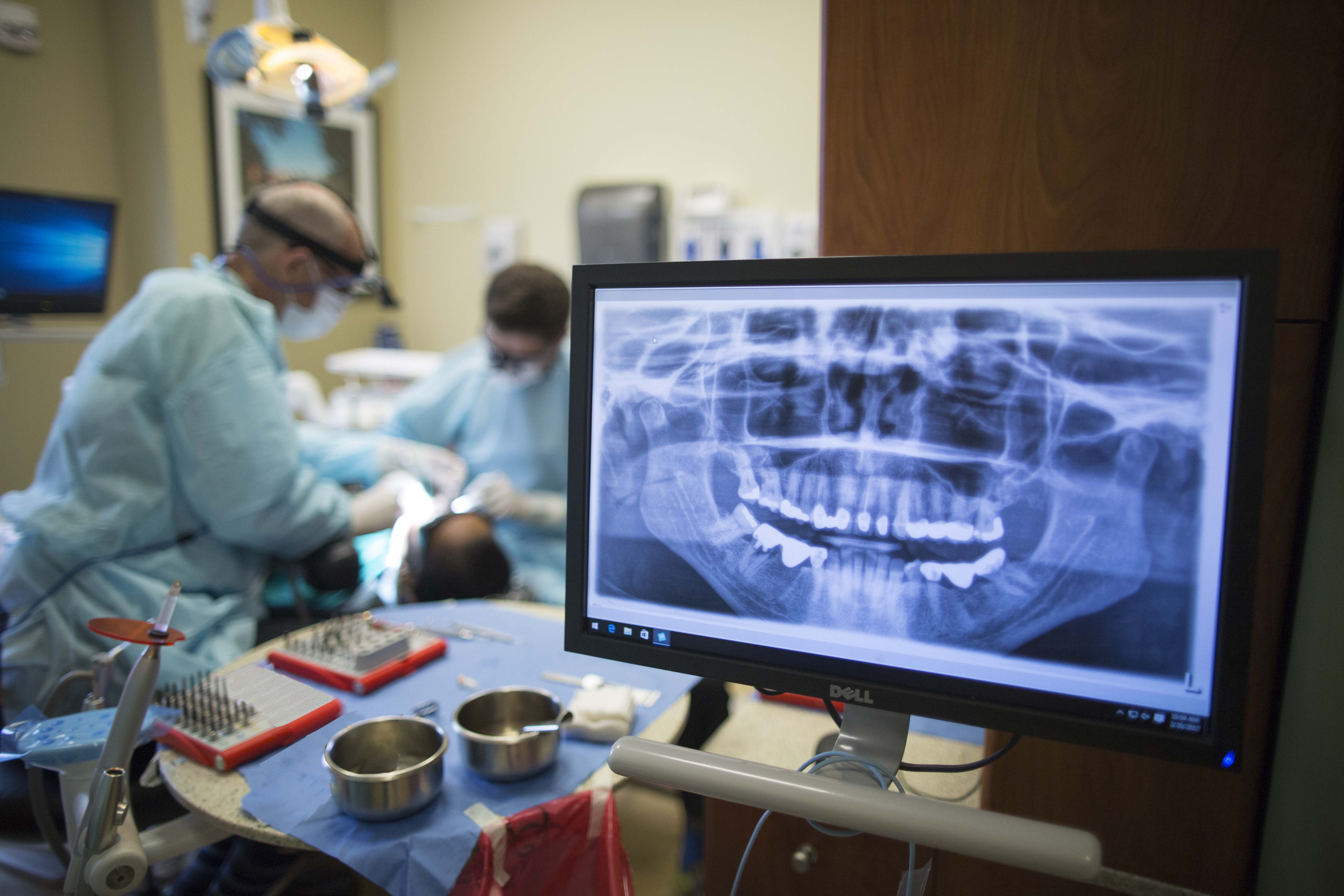 Dental x-ray shown on screen with two dentists working on a patient in the background