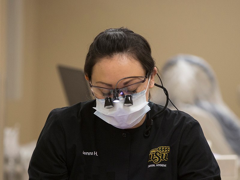Dental hygiene student looks down through magnification loupes