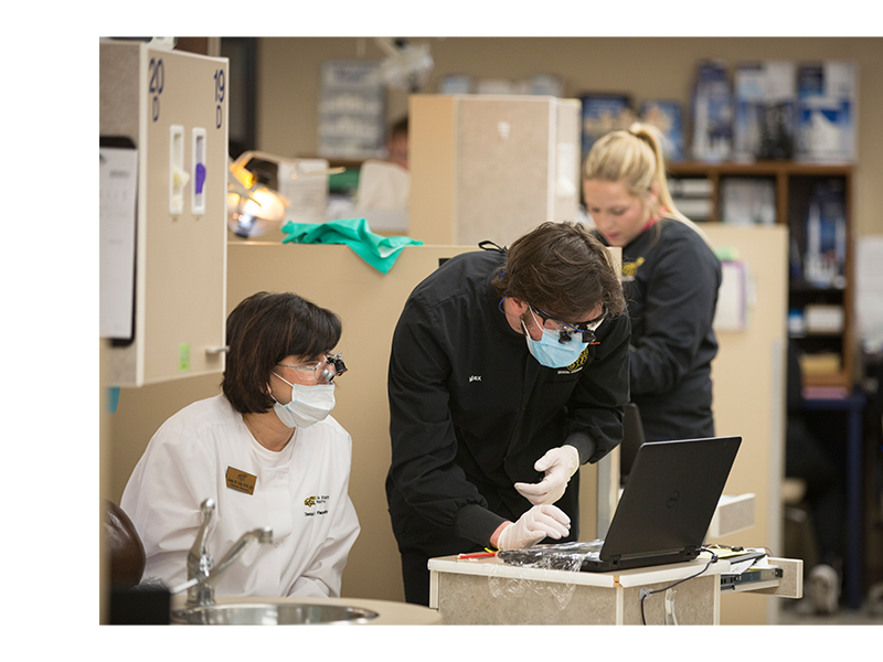 A dental hygiene male student and female instructor in the dental hygiene clinic looking at patient records on a laptop.