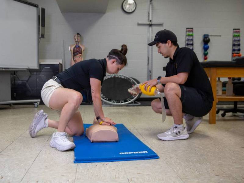 Students practice CPR techniques on a training mannequin in a clinical lab.