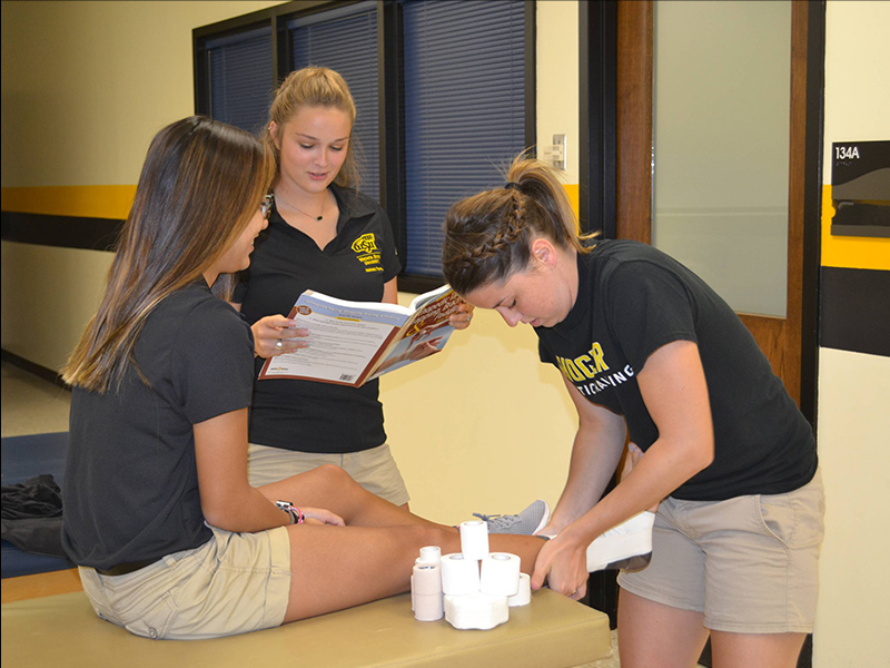 Students practice ankle taping in an athletic training lab.
