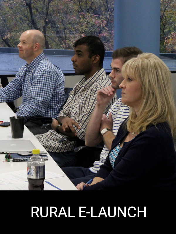 "Rural E-Launch" A group of people sit listening to someone explain the results of their customer interviews.