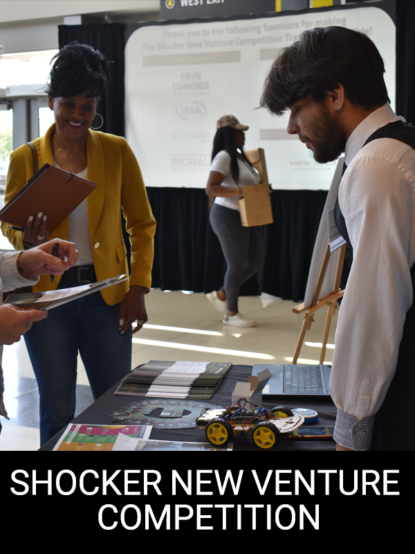 "Shocker New Venture Competition" A student stands at their booth presenting their idea to judges.