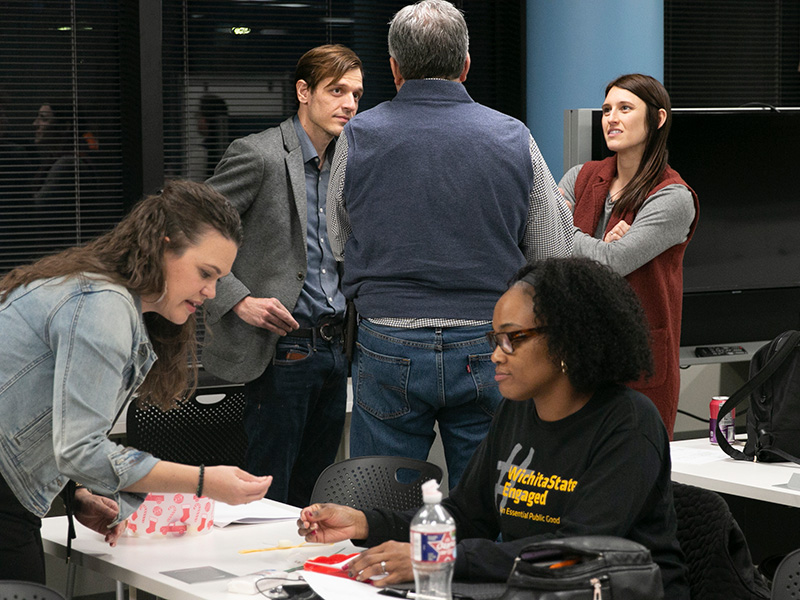 Two groups collaborating during a session of ignitor 1.0. One group stands talking while the other group is working with their hands.