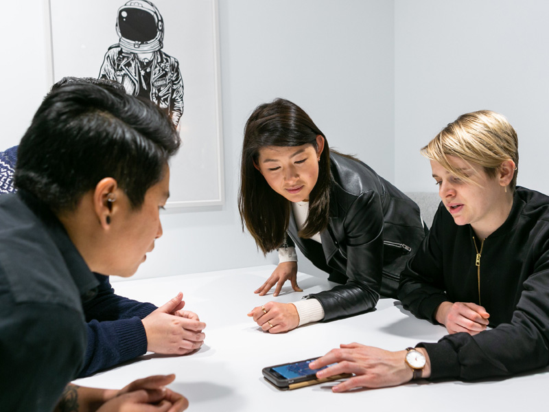 Three students talking and looking down at a phone.