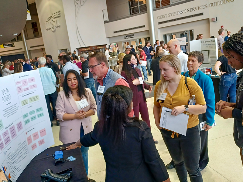 A group of judges visiting a booth interacts with the competitors.