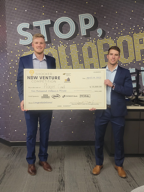 Jon Peterson and Jacob O'Connnor, the team members of Play Card, holding the giant $10,000 in front of the "Stop, Collaborate, Innovate" mural. 