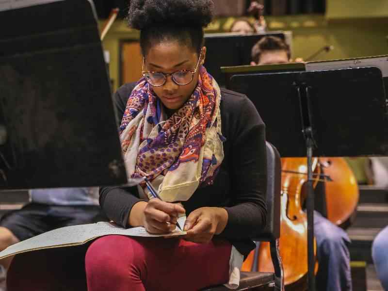 Female music major writing notes in sheet music.