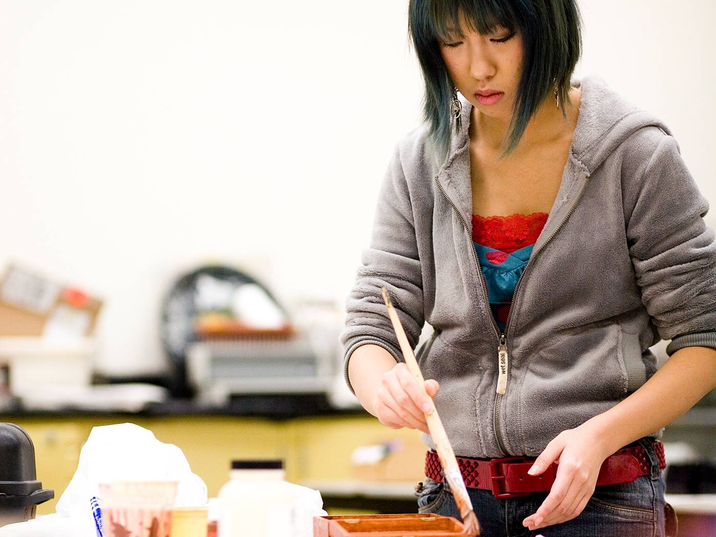 Student loading paintbrush with paint.