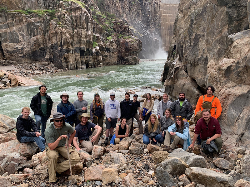 Students working in the field pose for a picture by a river.