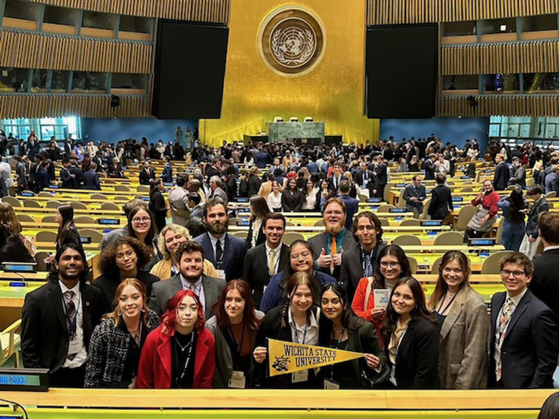 Students on a class trip pose with WSU pennants for a photo in an auditorium