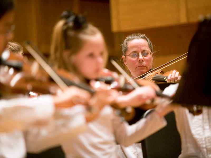 Instructor playing in an orchestra with students.