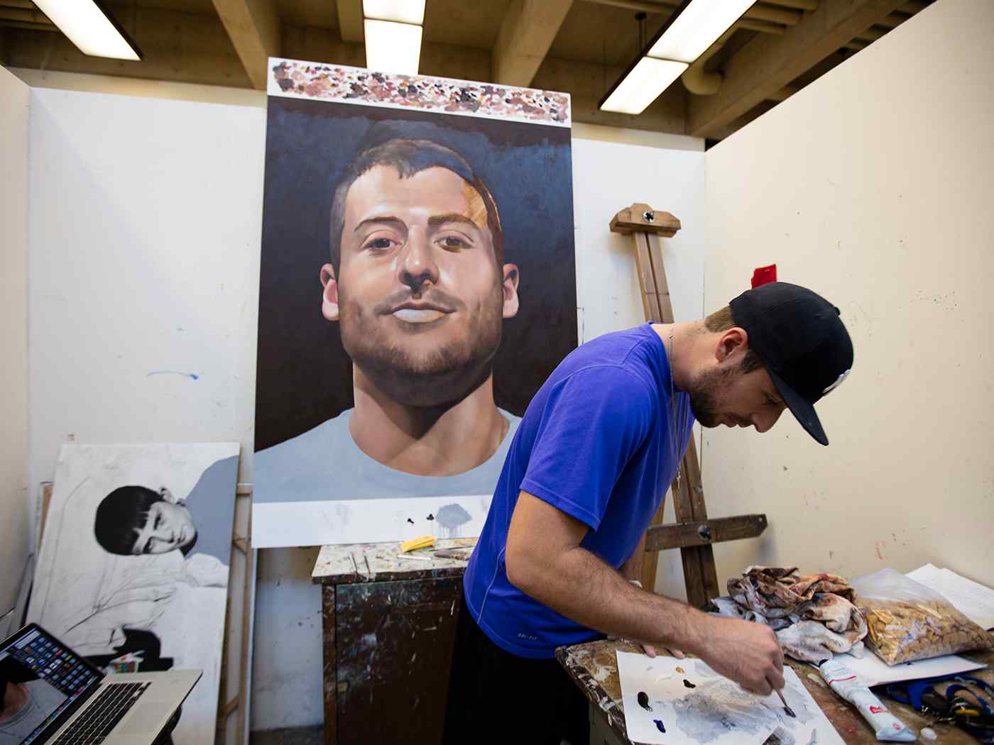 Student preparing paint to be used in a self-portrait on an easel. 