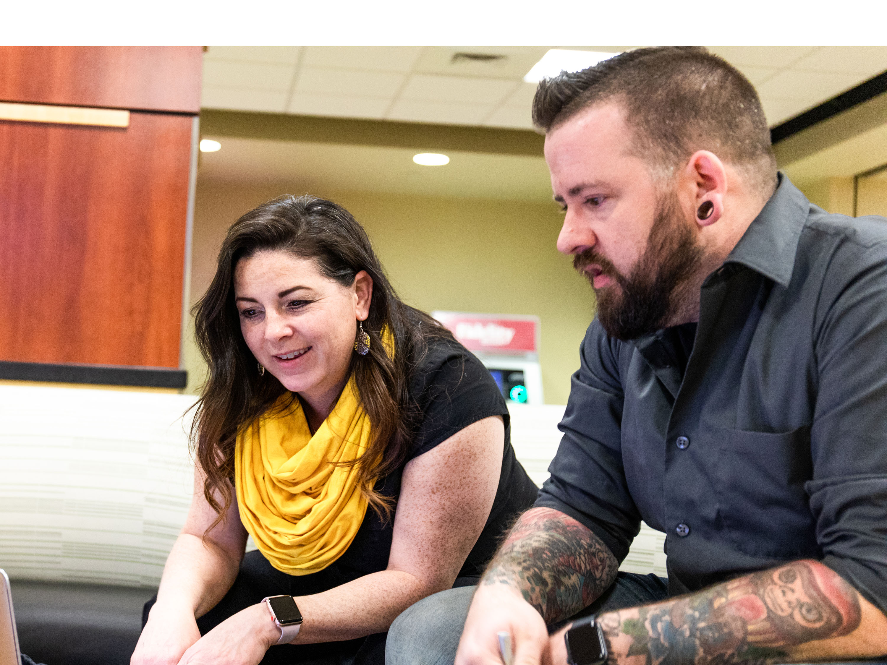 An image of two adult learners talking and looking at a laptop